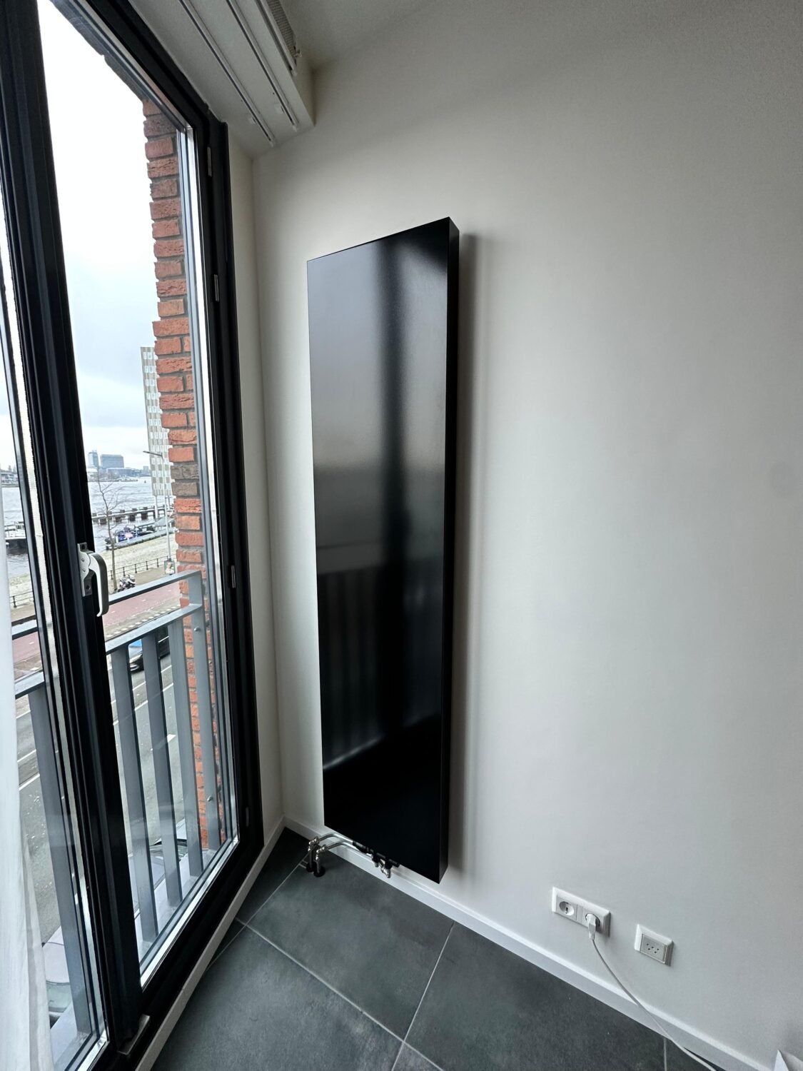 Zwarte verticale radiator naast een raam